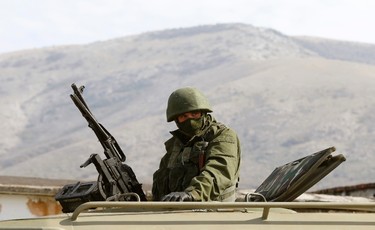 An armed man, believed to be a Russian serviceman, stands guard outside a Ukrainian military base in Perevalnoye, near the Crimean city of Simferopol, March 14, 2014. Russia shipped more troops and armour into Crimea on Friday and repeated its threat to invade other parts of Ukraine, showing no sign of listening to Western pleas to back off from the worst confrontation since the Cold War.  REUTERS/Vasily Fedosenko (UKRAINE - Tags: POLITICS MILITARY)