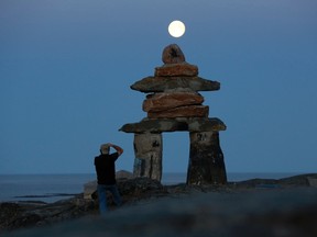 A man photographs a giant inukshuk as the moon rises above it in Rankin Inlet, Nunavut August 21, 2013.   REUTERS/Chris Wattie