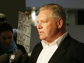 Doug Ford speaks to reporters while Chris Caple from the "Rob Ford Must Go" sit-in holds up a sign in the background at City Hall on Friday, March 28, 2014. (Michael Peake/Toronto Sun)