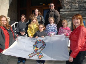 Shari Bishop, left, leader of the Autism support group for parents, and St. Thomas Mayor Heather Jackson, right, stretch out the Autism Awareness flag raised at city hall in 2012. Bailey Biship is front row centre. (File photo)