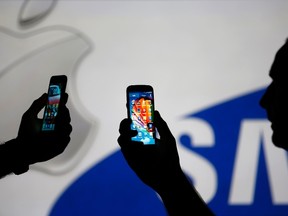 Men are silhouetted against a video screen with an Apple and Samsung logo as he poses with an Samsung S3 and Samsung S4 smartphone in this photo illustration taken in the central Bosnian town of Zenica, Aug. 14, 2013. REUTERS/Dado Ruvic