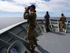 Gunner Richard Brown (L) of Transit Security Element looks through binoculars as he stands on lookout with other crew members aboard the Australian Navy ship HMAS Perth as they continue to search for missing Malaysian Airlines flight MH370. 
Australian Defence Force/Handout via Reuters