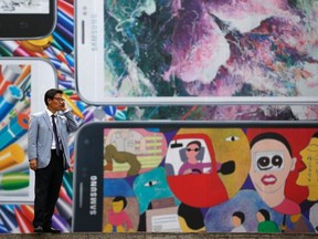 A man uses his mobile phone in front of a giant advertisement promoting Samsung Electronics' new Galaxy S5 smartphone, at an art hall in central Seoul April 15, 2014. Samsung Electronics Co Ltd's new Galaxy S5 smartphone should outsell its predecessor and defy predictions that the South Korean titan's latest model will struggle in a tough market for high-end handsets, Yoon Han-kil, senior vice president of Samsung's product strategy team, told Reuters in an interview. REUTERS/Kim Hong-Ji