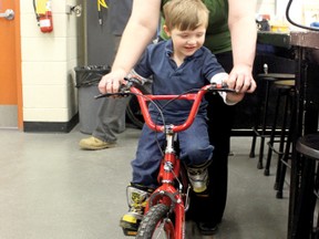 Brice Thorsteinson, 3, goes for his first-ever bike ride inside the shop class at Beaver Brae as his mother Sandra holds his bike upright until the training wheels can be put on.