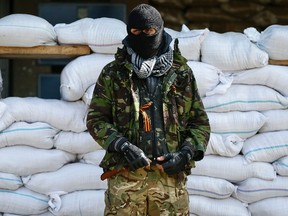An armed man, who is wearing black and orange ribbons of St. George - a symbol widely associated with pro-Russian protests in Ukraine, stands guard in front of barricades outside the mayor's office in Slaviansk on April 18, 2014. (REUTERS/Gleb Garanich)