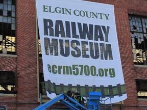 Workers from McBain Signs install a banner at Elgin County Railway Museum, where 10 huge historic railway photos also are to be put up on the exterior of the Wellington St. building. The museum is asking the public for images. (Dawn Miskelly, Elgin County Railway Museum)