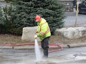 John Lappa/The Sudbury Star
A city worker uses a pressurized water hose to clean the sidewalk 
of mud and debris on Frood Road in Sudbury on Friday. A section of 
the road was closed Thursday night after a beaver dam gave way.