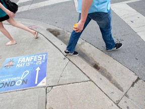 Pedestrians walk past a sign on the sidewalk directing foot traffic to the Memorial Cup Fan Fest in Jubilee Square, between Budweiser Gardens and the Covent Garden Market. (CRAIG GLOVER/The London Free Press)