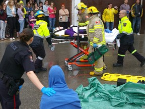An Aylmer police officer with her hand on a student driver she has arrested, watch as an injured passenger is wheeled to an ambulance in the aftermath of a dramatization of a deadly crash caused by distracted driving, Thursday in Aylmer at East Elgin Secondary School.