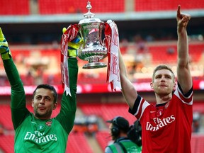 Arsenal goalkeeper Lukasz Fabianski (left) and teammate Per Mertesacker lift the trophy to celebrate their victory against Hull City in the FA Cup final at Wembley Stadium in London, May 17, 2014.                  (REUTERS/Darren Staples)