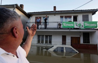 A man waves to his neighbours during heavy floods in Bosanski Samac May 19, 2014. Bosnia said on Monday that more than a quarter of its 4 million people had been affected by the worst floods to hit the Balkans in living memory, comparing the "terrifying" destruction to that of the country's 1992-95 war. The extent of the devastation became apparent in Serbia too, as waters receded in some of the worst-hit areas to reveal homes toppled or submerged in mud, trees felled and villages strewn with the rotting corpses of livestock. REUTERS/Srdjan Zivulovic