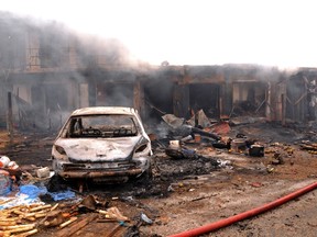 The wreckage of a charred vehicle remains in front of burning shops following a bomb blast at Terminus market in the central city of Jos on May 20, 2014. Twin car bombings on Tuesday killed at least 46 in central Nigeria in the latest in a series of deadly blasts that will stoke fears about security despite international help in the fight against Boko Haram Islamists. AFP PHOTO / STR