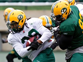 Running back Aaron Milton, left, is grabbed by defensive tackle Don Oramasionwu during camp at Commonwealth Stadium Thursday. (Codie McLachlan, Edmonton Sun)