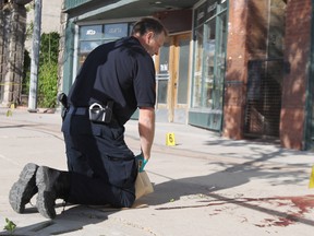A Winnipeg Police Service forensic identification officer collects evidence at the scene of a stabbing on Main Street between Logan and Alexander Avenues which happened at about 3:30 p.m. on Sat., June 7, 2014. Police say an adult male was transported to hospital in critical condition, while another adult male was in custody. (Kevin King/Winnipeg Sun/QMI Agency)