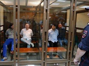 Defendants in the murder trial of Russian journalist and human rights activist Anna Politkovskaya, (L-R) Ibragim Makhmoudov, Lom-Ali Gaitukayev, Dzhabrail Makhmoudov, Rustam Makhmoudov and Sergei Khadzhikurbanov sit inside a glass-walled cage, while a policeman stands guard in the foreground, during a court hearing in Moscow, June 9, 2014. REUTERS/Sergei Karpukhin