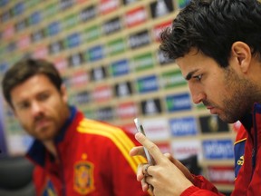 Spain's Xabi Alonso (L) looks at teammate Cesc Fabregas using his mobile phone at the start of a news conference at the Spanish Soccer Federation headquarters in Las Rozas, outside Madrid October 15, 2012. (REUTERS/Susana Vera)