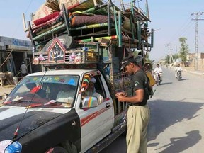 A policeman (R) checks an identification card of residents travelling with their belongings on a vehicle, fleeing a military offensive against Pakistani militants in North Waziristan, as they enter at a checkpoint in Bannu, Pakistan's Khyber-Pakhtunkhwa province June 13, 2014. REUTERS/Zahid Mohammad