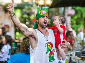 Andre Camara, holding his 9-month-old son Joao-Christiano Camara, cheers on as he watches the Portugal-Germany World Cup game screened at Bairrada Churrasqueira Grill on College St. in Toronto on Monday, June 16, 2014. (Ernest Doroszuk/Toronto Sun)