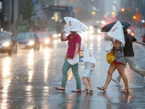 People are pictured crossing Bloor St. in heavy rain last July. Environment Canada is warning people to prepare for heavy rain and thunderstorms on Tuesday. (CRAIG ROBERTSON, Toronto Sun)