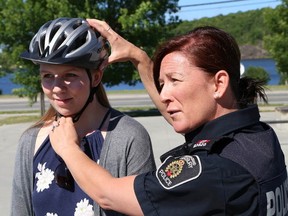 JOHN LAPPA/THE SUDBURY STAR
Const. Cheryl Kennelly, of the Greater Sudbury Police, demonstrates how to wear a bicycle helmet properly with the help of summer student Maija Hirvi at the launch of the Helmet Awareness Campaign at the Minnow Lake Skate Park on Thursday. The Brain Injury Association Sudbury and District and Health Sciences North emergency department have teamed up to promote the BIASD's campaign. The campaign features $15 vouchers that can be used toward the purchase of a new helmet from local stores such as Canadian Tire stores in Sudbury and Espanola, Adventure Ski and Cycle, Pinnacle Sports, Skater's Edge and Greenhawk Harness and Equestrian. The campaign was created to raise awareness about brain injuries and to encourage the use of helmets.