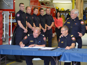 Captain Don Degenhardt (right) signs over his platoon to new Captain Rob Good (left). Smiling platoon members and deputy fire chief Tim Vandenbrink (top right) look on. - Caitlin Kehoe Reporter/Examiner