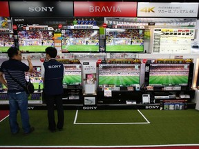 A shopper (L) looks at Sony Corp's Bravia television sets screening a soccer match at an electronics retail store in Tokyo June 10, 2014.  REUTERS/Issei Kato