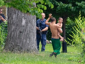 A man keeps one hand in the air as he carries a child with the other while being evacuated by the London Police's Emergency Response Unit from a Queens Avenue home after a passerby called 911, reporting a person was pointing what they believed to be a firearm at passing vehicles, in London, Ontario on Monday June 30, 2014.  Police blocked off Queens Avenue between Quebec and Ontario Streets as they went door-to-door searching for a suspect.  After nearly two hours, police determined there was no threat to public safety, reopening the street and allowing residents to return to their homes.
(CRAIG GLOVER/The London Free Press/QMI Agency)