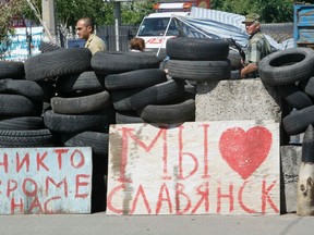 An armed pro-Russian separatist (R) stands guard at a checkpoint in the Ukrainian eastern city of Slaviansk July 1, 2014. The board (C) reads, "We love Slaviansk". REUTERS/Shamil Zhumatov