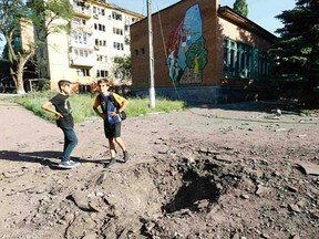 Boys stand near a shell crater outside a local school in the eastern Ukrainian town of Kramatorsk July 1, 2014. REUTERS/Shamil Zhumatov