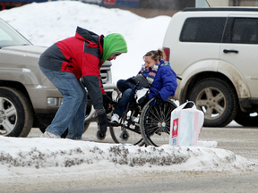 A good Samaritan (left) helps a woman in a wheelchair who became stuck in the ice and snow while crossing 116 Street at 104 Avenue, in Edmonton, Alta., on Friday Dec. 20, 2013. (David Bloom/Edmonton Sun)