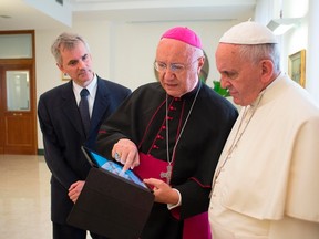 Pope Francis, right, watches as Archbishop Claudio Maria Celli, centre, president of the Pontifical Council for Social Communications, shows him news on a tablet during a meeting at the Vatican July 7, 2014. (REUTERS/Osservatore Romano)