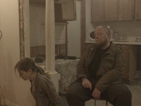 A handcuffed Grace (Nikki Garrett) kneels on the floor as gang member Marv (Thom Fairley) keeps an eye on her in a scene from the shot-in-Kingston, post-apocalyptic thriller The Stronghold.