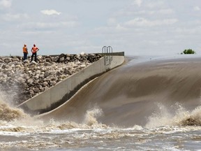 Officials survey the spillway as dozens of pieces of heavy machinery work to raise the dike on the Portage diversion, to divert floodwaters from the rising Assinibione river near Portage La Prairie, west of Winnipeg, Manitoba July 9, 2014. (REUTERS/Lyle Stafford)