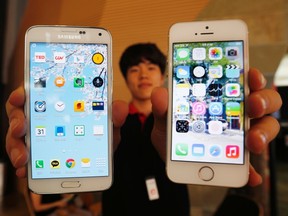 A sales assistant holding Samsung Electronics' Galaxy S5 smartphone (L) and Apple Inc's iPhone 5 smartphone (R) poses for photographs at a store in Seoul July 16, 2014. REUTERS/Kim Hong-Ji
