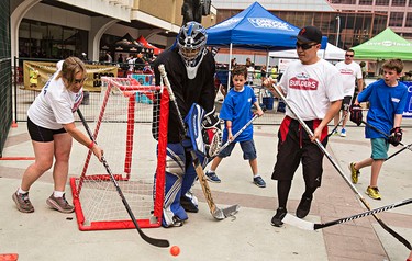 Players attack goaltender Luis Torres' net during the Five Hole for Food ball hockey tournament at Centennial Plaza in Edmonton, Alta., on Wednesday, July 16, 2014. The aim of the tournament is to gather donations for local food banks. Edmonton is the 11th stop out of 13 on this year's tour. Codie McLachlan/Edmonton Sun/QMI Agency