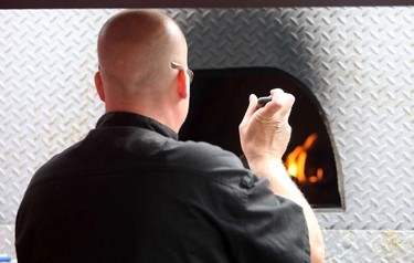 Jason Paquette with Canicus Wood Fired Pizza checks his pies in a wood buring oven built in a converted fire truck during the opening day for Taste of Edmonton at Churchill Square in Edmonton, Alberta on July 17, 2014.  Perry Mah/Edmonton Sun/QMI Agency