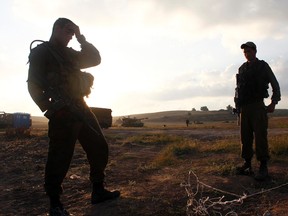 Israeli soldiers stand in a field outside the southern Gaza Strip July 17, 2014. Palestinians rushed to shops and banks on Thursday as a five-hour humanitarian truce agreed by Israel and Hamas came into force, hours after the Israeli military said it had fought off gunmen who infiltrated from Gaza. REUTERS/Ronen Zvulun