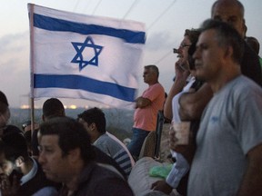 Israeli, mostly residents of the southern Israeli city of Sderot, stand with an Israeli flag on a hill overlooking the Gaza Strip, on July 20, 2014, to watch the fighting between the Israeli army and Palestinian militants. (AFP PHOTO / JACK GUEZ)