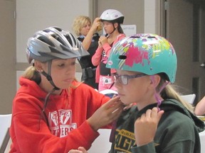 Megan Hakr, left, adjusts the bicycle helmet of Alexis Seller-VanSickle during Cop Camp for Kids, at the Chatham-Kent Children's Safety Village. At back, Special Cst. Randi Hull adjusts the helmet of her daughter, Kamryn.