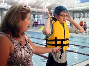 Barbara Costache, chief administrative officer with the Lifesaving Society of Alberta and Northwest Territories, demonstrates with Chelsea Brooks, 19, right, how to properly put on a life jacket at the unveiling of a  new provincial public awareness beach towel campaign reminding Albertans to take the proper steps to prevent drowning this summer at the MacEwan University Pool, 10800 104 Ave NW in Edmonton, AB on July 24, 2014. TREVOR ROBB/Edmonton Sun
