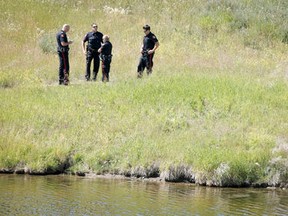 Police stand near a pond at the corner of 16 Ave. and Stoney Tr. N.E. in Calgary, Alta., on Thursday, July 24, 2014. A body was found in a storm water pond at the intersection. Lyle Aspinall/QMI Agency