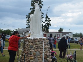 A woman (bottom left) bows her head in prayer as she touches a statue of St. Anne, during the Lac Ste. Anne Pilgrimage on July 20. - Caitlin Kehoe, Reporter/Examiner