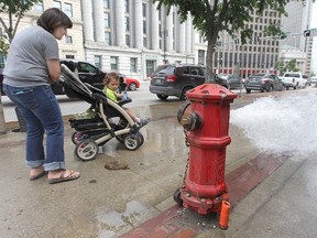 Pedestrians stop to look at an open fire hydrant on Main Street near McDermot Avenue on Saturday. (Kevin King/Winnipeg Sun)