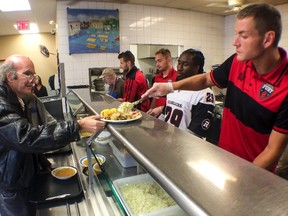 Omar Jarun (right), a defender with the Ottawa Fury FC, serves a client lunch at the Shepherds of Good Hope as Ottawa RedBlacks RB Chevon Walker looks on Monday, July 28, 2014. Errol McGihon/Ottawa Sun/QMI Agency