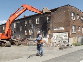 Jim Moodie/The Sudbury Star
A worker with Lacroix Construction positions a section of security fence while an excavator removes bricks from the side of an apartment building at the corner of Pine and Elm streets. Dalron, the new owner of the property, is tearing down the notorious roominghouse and will create a parking lot in its place, with an eye to redeveloping the lot as a commercial/retail building in the future.