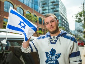 Former Israeli soldier Ilan Mann, 25,  poses for a photo with his car adorned with two Israeli flags in downtown Toronto. (ERNEST DOROSZUK, Toronto Sun)