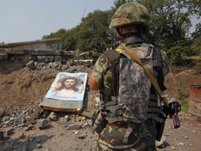 A Ukrainian serviceman stands near a damaged board with an image of Jesus Christ, which was left by pro-Russian separatists, at a check point in the town of Vuhlehirsk, Donetsk region, August 14, 2014. (REUTERS/Valentyn Ogirenko)