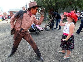 Ava Frayn, 7, interacts with the Copper Cowboy (Daniel Anderson) during the Edmonton International Fringe Festival in Old Strathcona Sunday. (David Bloom/Edmonton Sun)
