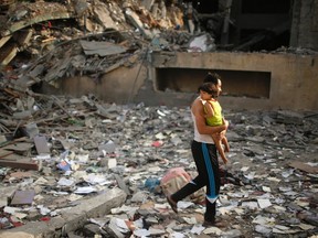 A Palestinian man holding his child walks near the remains of one of Gaza's tallest apartment towers, which witnesses said was hit by an Israeli air strike that destroyed much of it, in Gaza City August 26, 2014. REUTERS/Mohammed Salem