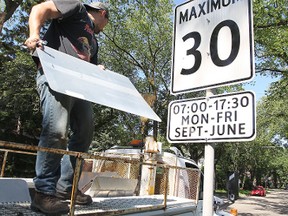 Ryan Laurin with the City of Winnipeg's Traffic Services division removes a cover from a school zone speed limit sign near Dorchester School in Crescentwood last summer. Reduced speed limits in school zones during certain times will be expanded to another 120 areas throughout the city early next year. (Kevin King/Winnipeg Sun file photo)